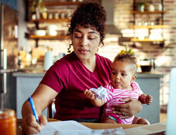 Mother holding a baby while writing at a kitchen table